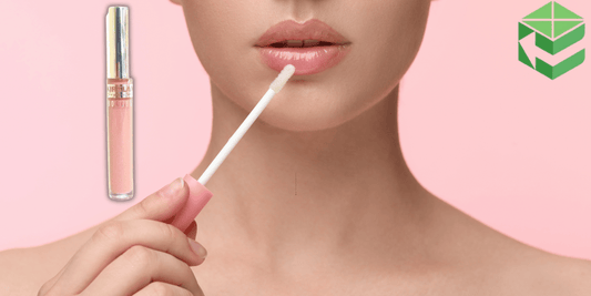 A close-up of a woman applying Kirkland Signature Borghese Mineral Lip Shine Nude. The lip gloss tube is displayed separately on a soft pink background, with a glossy finish on the lips.